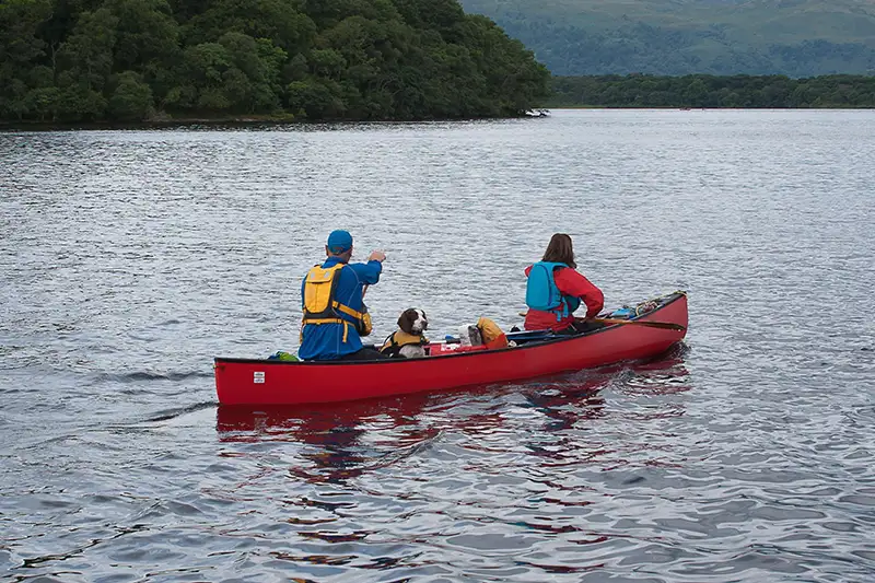 Deux personnes pagayant en canoë sur un loch en Écosse avec un chien