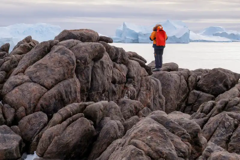 Touriste sur des roches entourées de glace en Antarctique