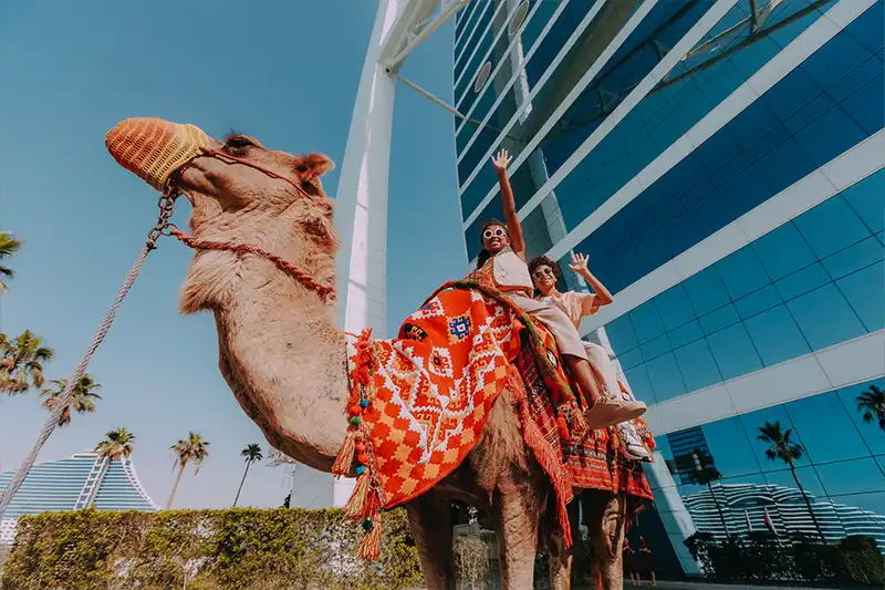 Activités familiales exclusives – Burj Al Arab Jumeirah Famille en balade à dos de chameau devant le Burj Al Arab