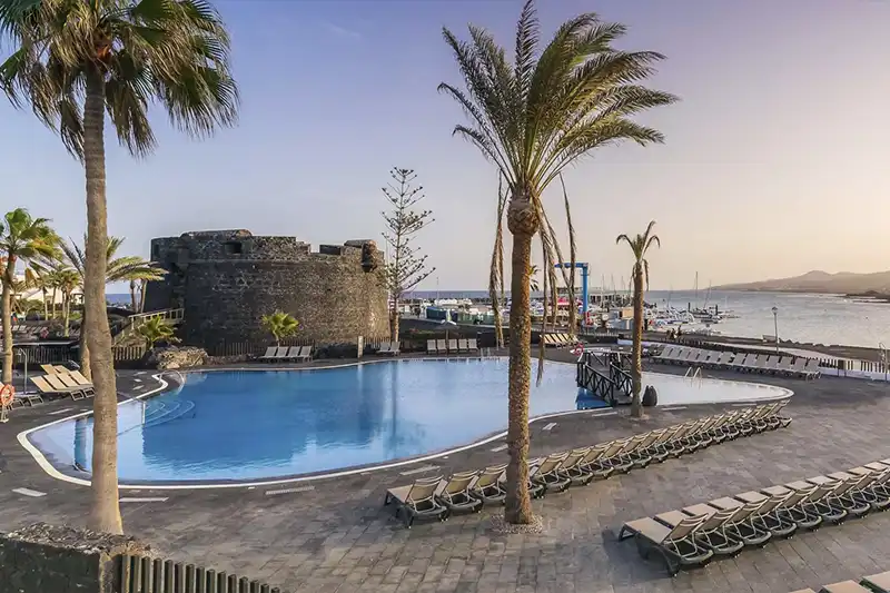 Piscine extérieure du Barceló Castillo à Fuerteventura, entourée de palmiers et de transats.