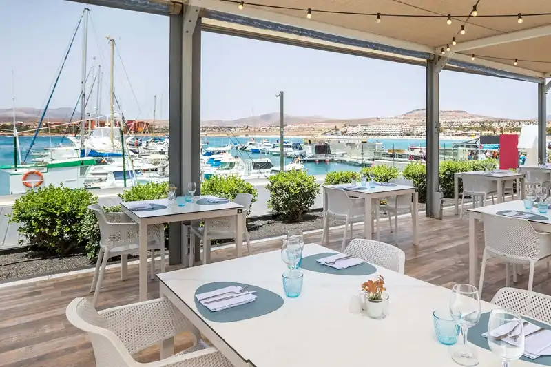 Terrasse de restaurant avec tables dressées et vue sur la marina à Fuerteventura.