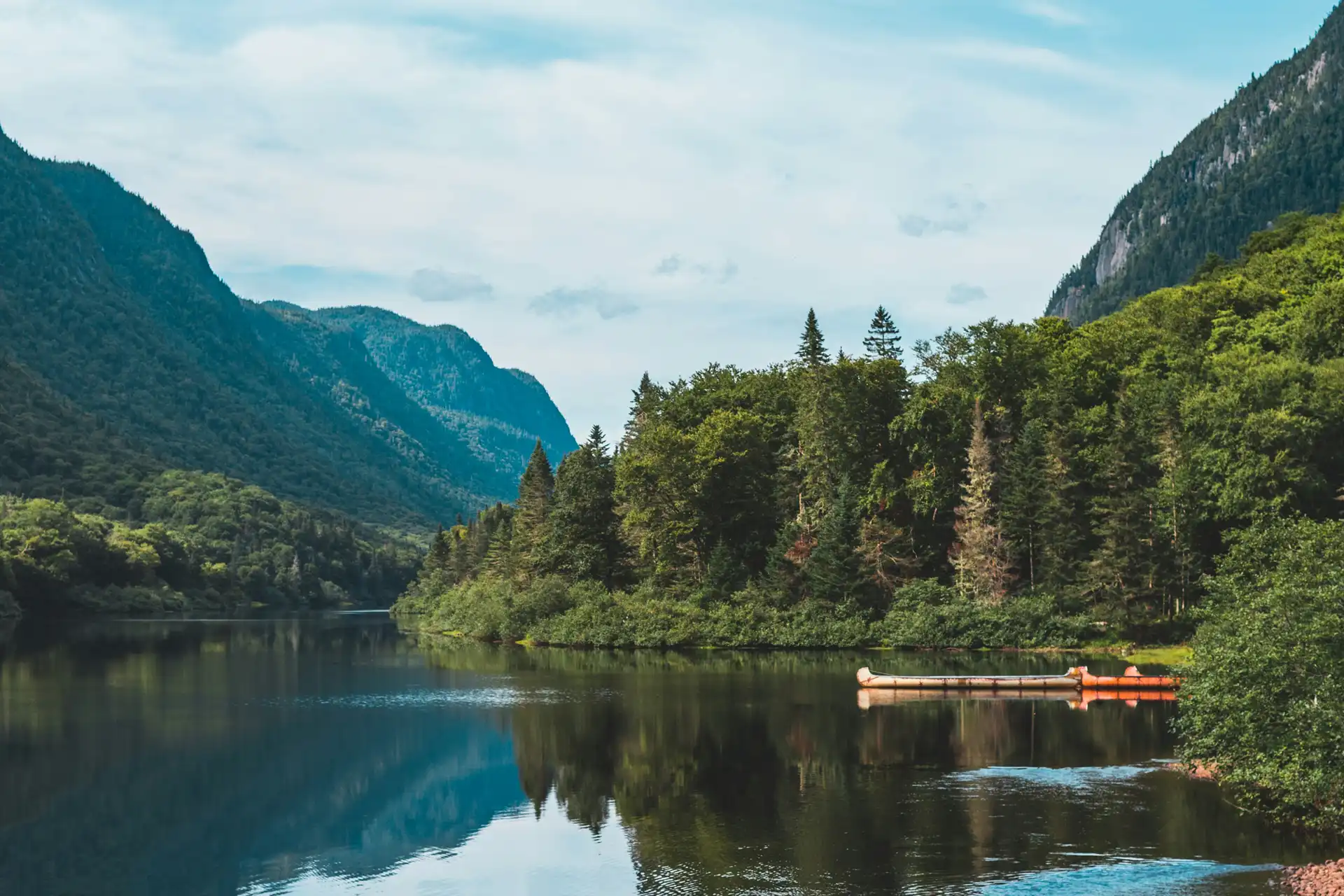Le Canada autrement – Autotours 2027 Lac entouré de montagnes boisées et de forêts, avec des canots sur l'eau