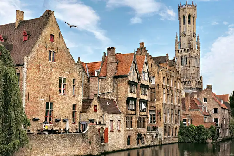Maisons médiévales au bord d’un canal avec le beffroi de Bruges en arrière-plan
