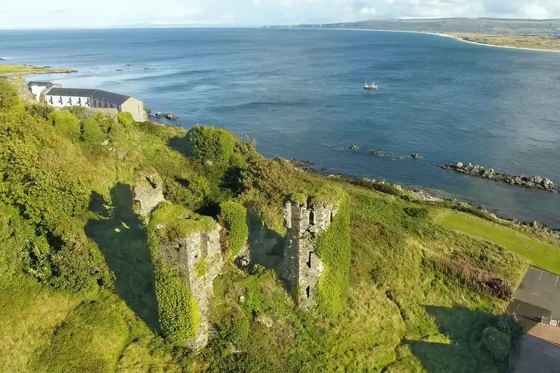 Ruines d'un château de pierre sur une côte verdoyante, face à la mer en Irlande