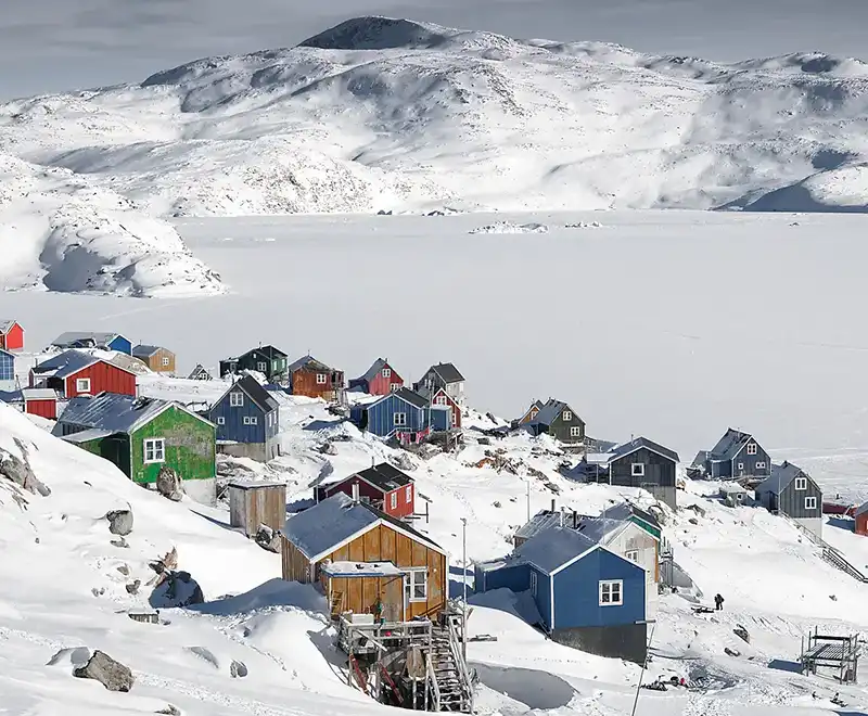 Village groenlandais enneigé avec maisons colorées au bord d’un paysage glacé
