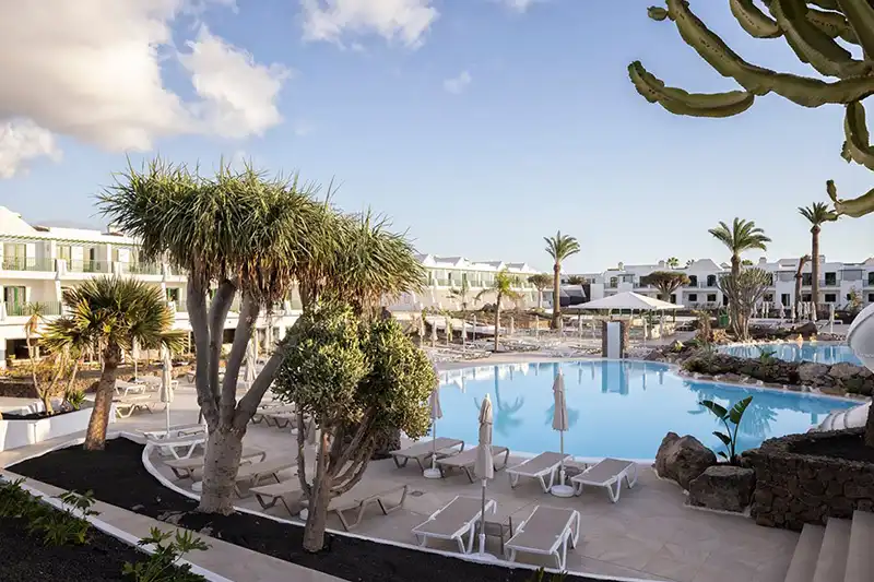 Grande piscine extérieure entourée de transats, de palmiers et de jardins au MYND Yaiza.