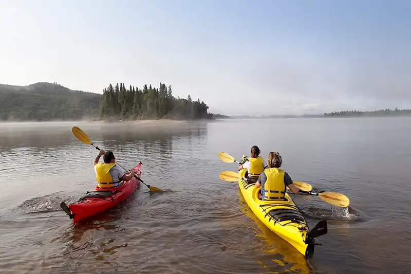 Deux kayaks avec leurs occupants naviguant sur un lac bordé de forêts au Canada.