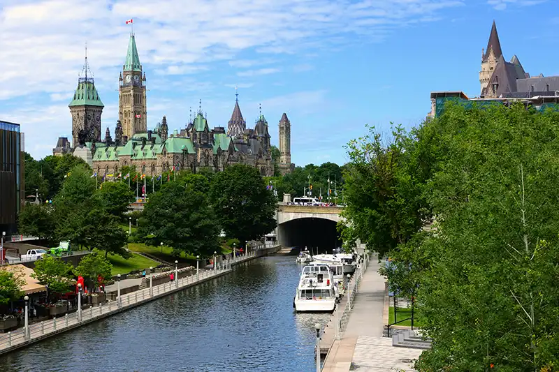 Vue du Parlement canadien et du canal Rideau à Ottawa, bordé de promenades et d'espaces verts.