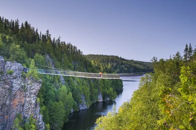Passerelle suspendue au-dessus d'un lac entouré de falaises et de forêts dans le parc national d'Aiguebelle, au Québec.